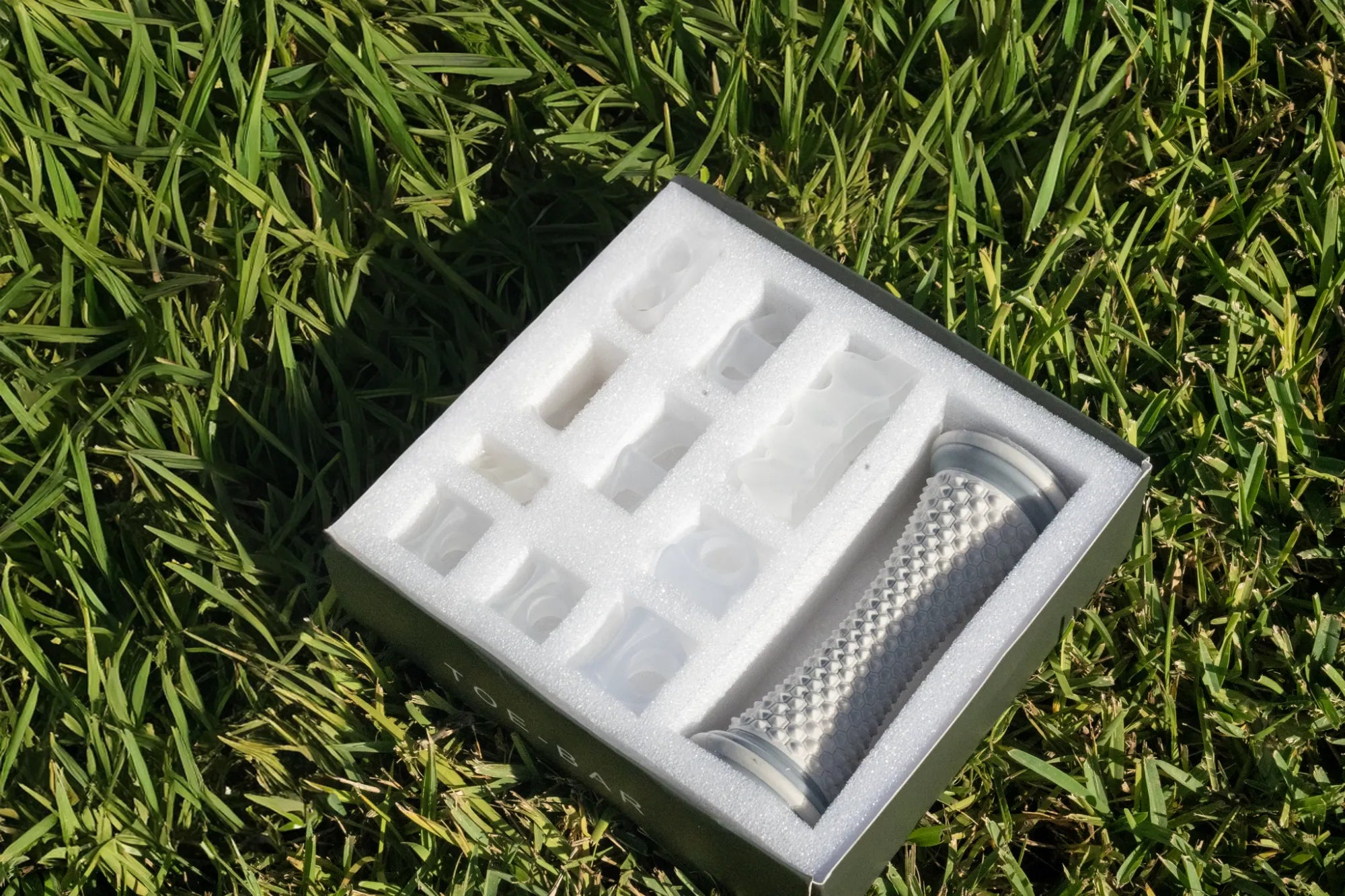 Toe-Bar Balance Kit open box showing foam-molded tray with silicone toe correctors and foot roller on grass