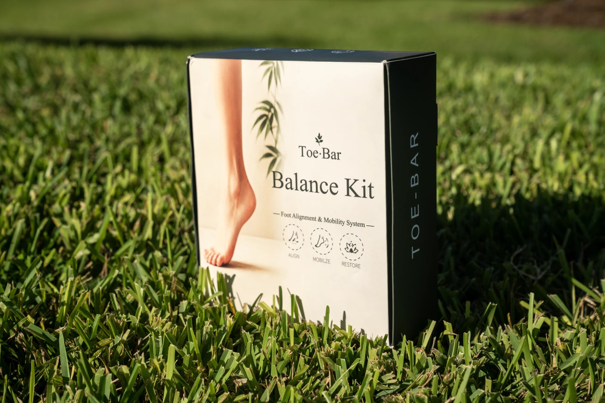 Toe-Bar Balance Kit box standing upright on grass showing front packaging with foot and bamboo design